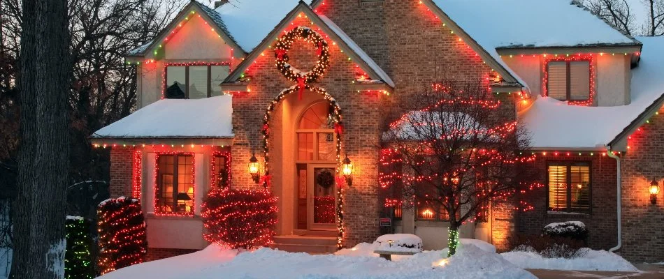 Red holiday lights on a home with snow in Olathe, KS.